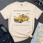Ivory Comfort Colors t-shirt with a yellow taxi graphic and text  on a dark surface with a denim jacket and a map.