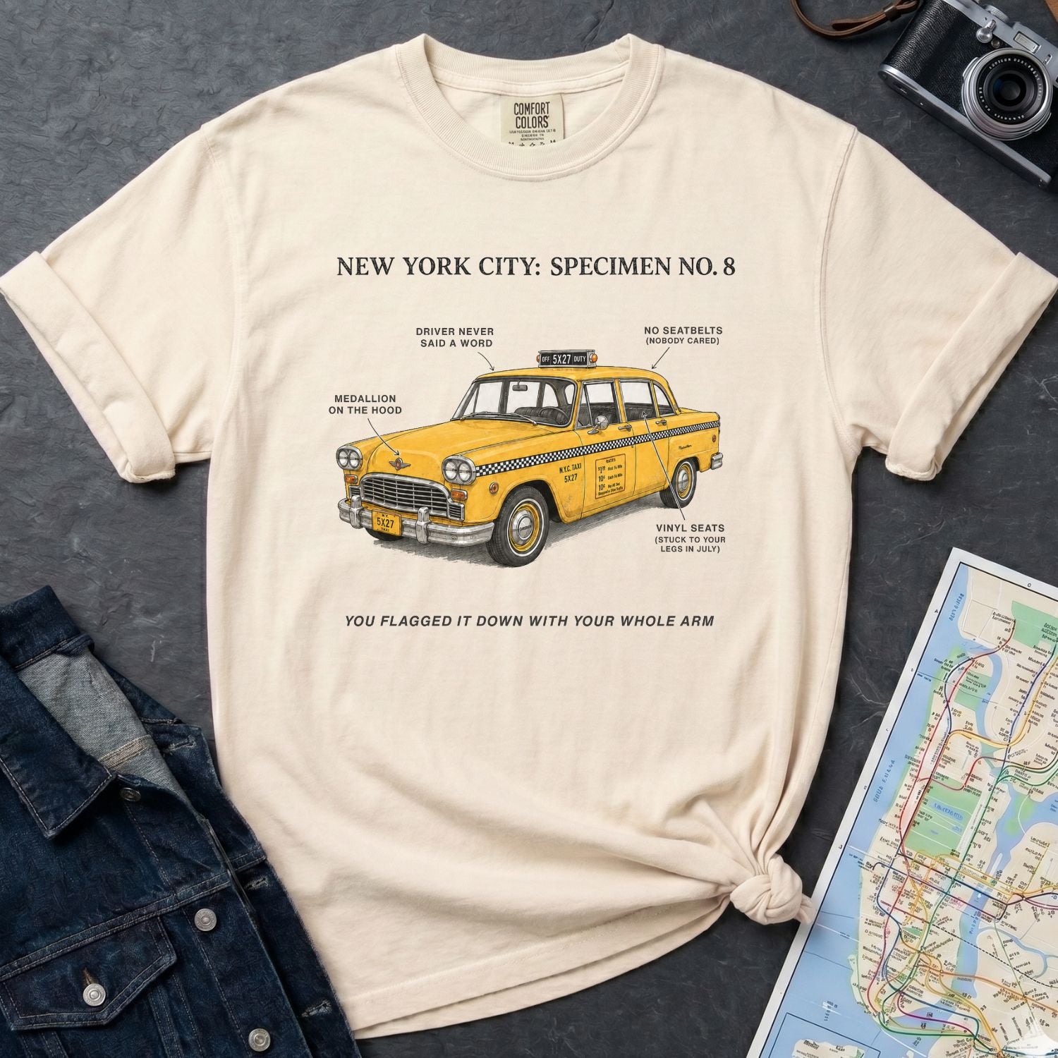 Ivory Comfort Colors t-shirt with a yellow taxi graphic and text  on a dark surface with a denim jacket and a map.