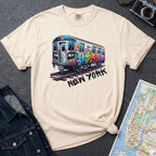 Ivory t-shirt with a colorful train graphic and 'New York' text on a gray surface with a map and denim jacket.