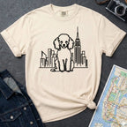 Ivory t-shirt with a poodle and cityscape design on a dark surface with a map and camera.