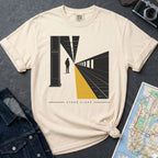 Ivory Comfort Colors t-shirt with a graphic design of a train station platform and text 'Stand Clear' on a dark surface with a denim jacket and a map.