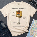 Ivory Comfort Colors t-shirt with a graphic design of a vintage intersection crossing sign and text, placed on a dark surface with a denim jacket and a map.