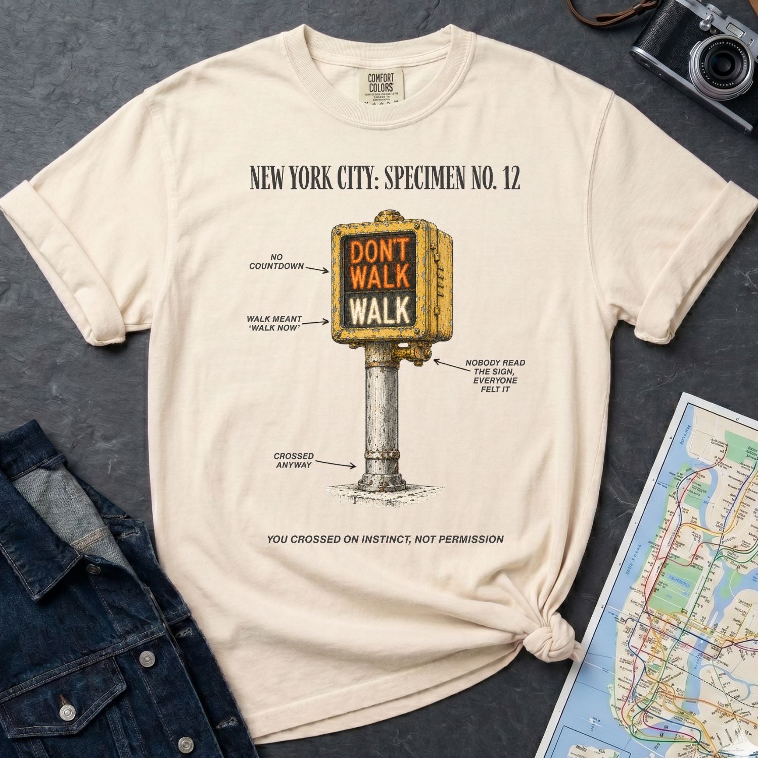 Ivory Comfort Colors t-shirt with a graphic design of a vintage intersection crossing sign and text, placed on a dark surface with a denim jacket and a map.