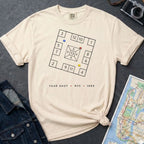 Ivory Comfort Colors t-shirt with New York City skelzies design on a gray surface with denim jacket and map.