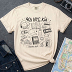 Ivory Comfort Colors t-shirt with '90s NYC Kid' graphic design on a dark surface with denim jacket and map.