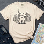 Ivory Comfort Colors t-shirt featuring a minimalist Shiba Inu graphic in front of the New York City skyline on a dark surface with a denim jacket and a map.