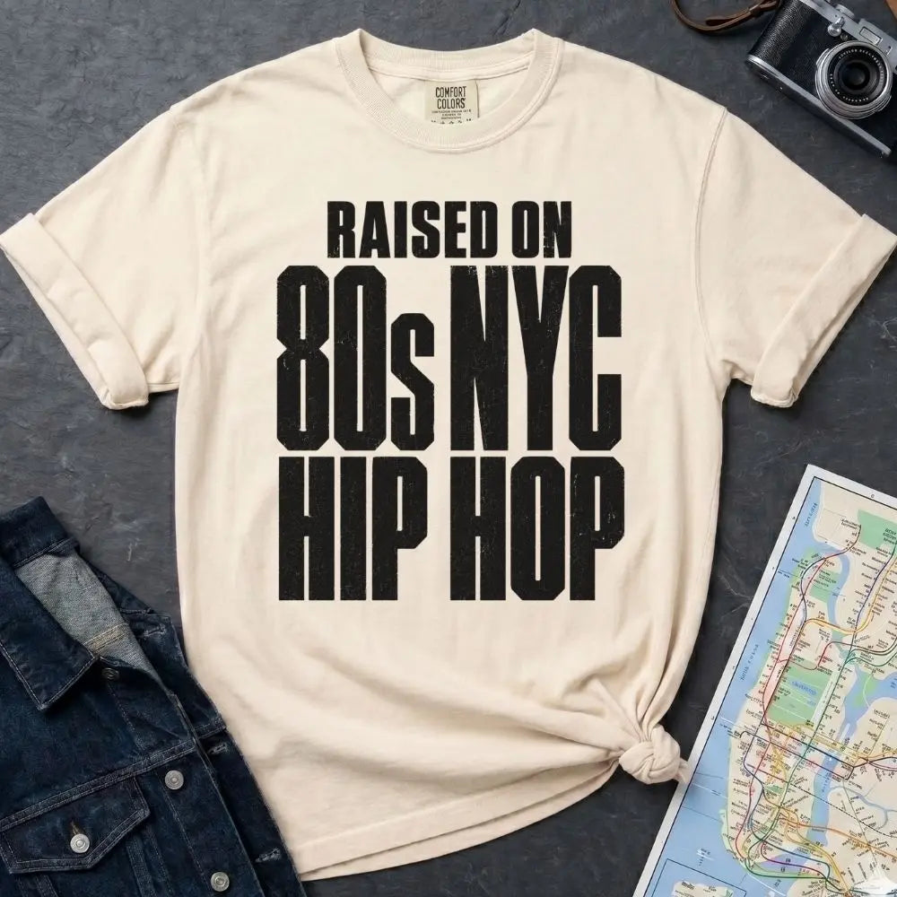 Ivory Comfort Colors T-shirt with black Raised on 80s NYC Hip Hop front print, styled with denim jacket, camera, and subway map
