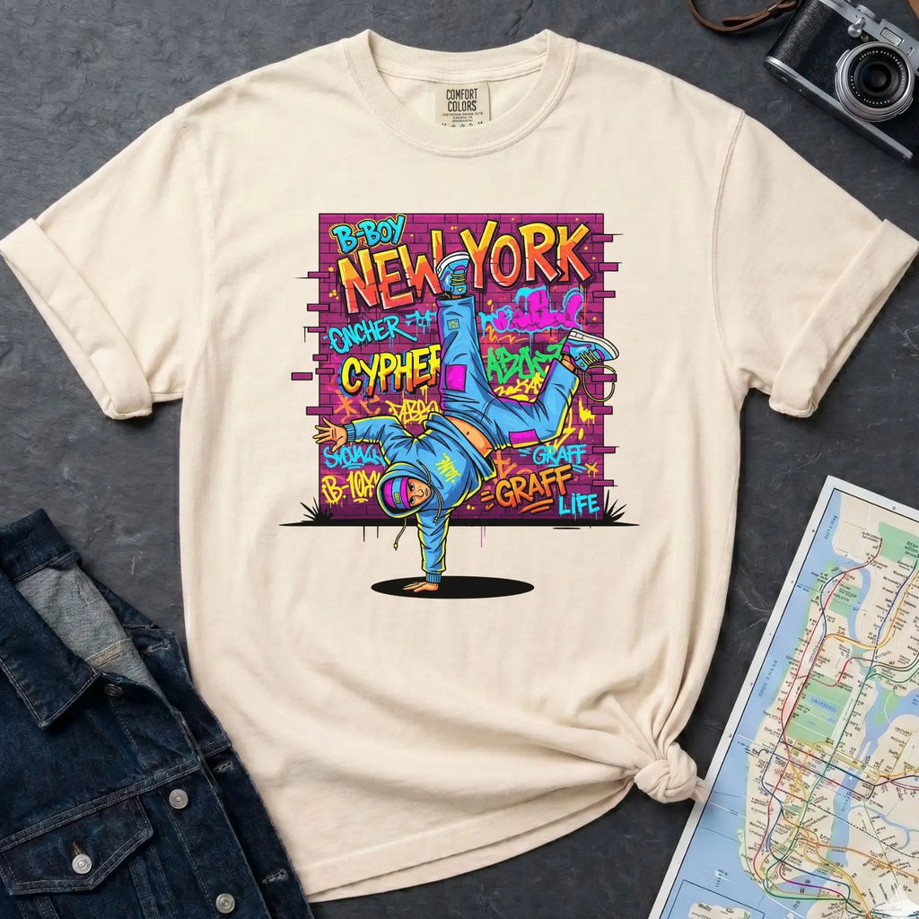 Ivory Comfort Colors t-shirt with a colorful graphic design featuring a breakdancer and text on a dark surface with a denim jacket and a map.