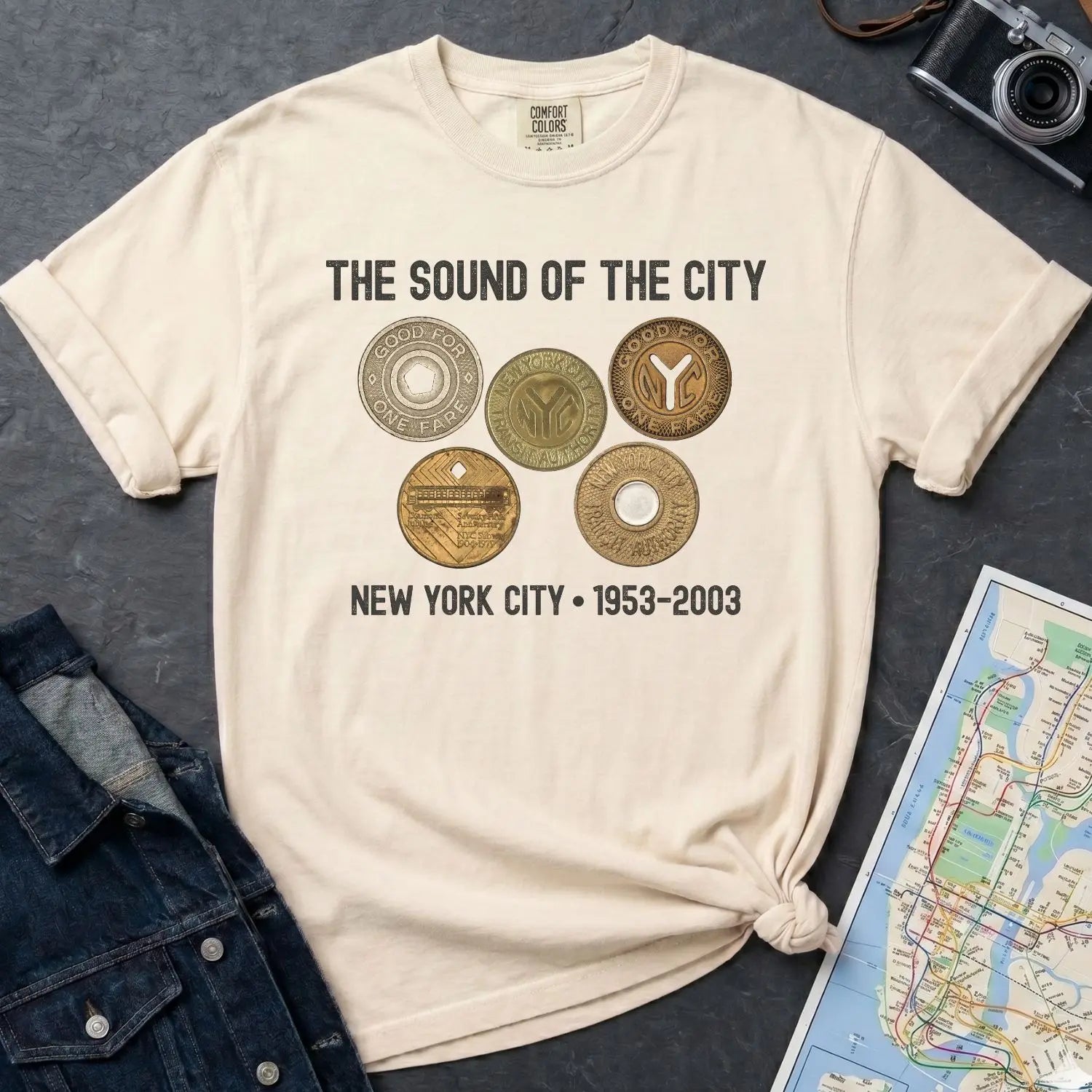 Ivory Comfort Colors t-shirt with 'The Sound of the City' design featuring vintage coins on a textured surface with a camera and map.