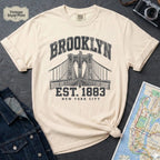 Ivory Vintage-style Brooklyn NYC graphic t-shirt on a Bay colored Comfort Colors cotton shirt, featuring the Brooklyn Bridge and “Brooklyn Est. 1883” text.