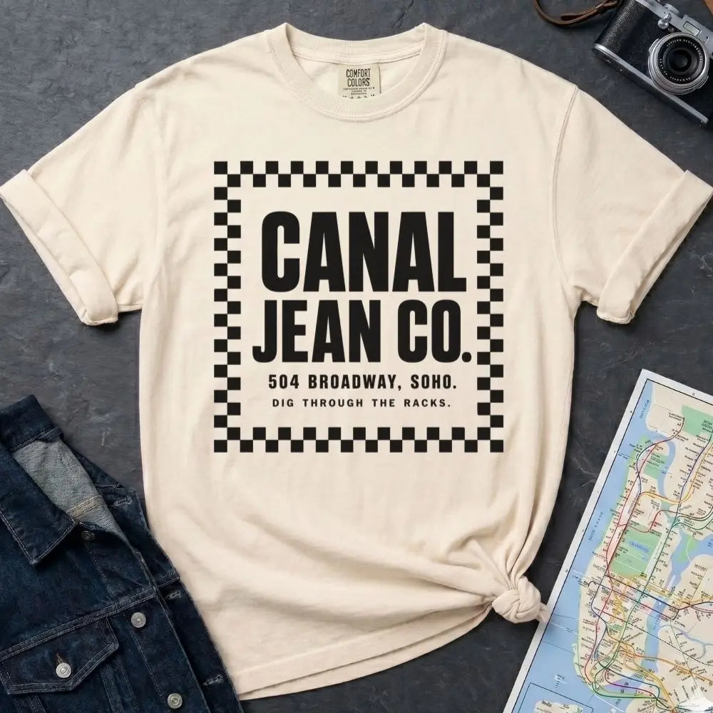 Ivory Comfort Colors T-shirt with black Canal Jean Co. NYC front print, styled with denim jacket, camera, and subway map.