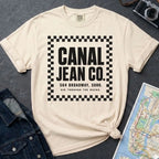 Ivory Comfort Colors T-shirt with black Canal Jean Co. NYC front print, styled with denim jacket, camera, and subway map.