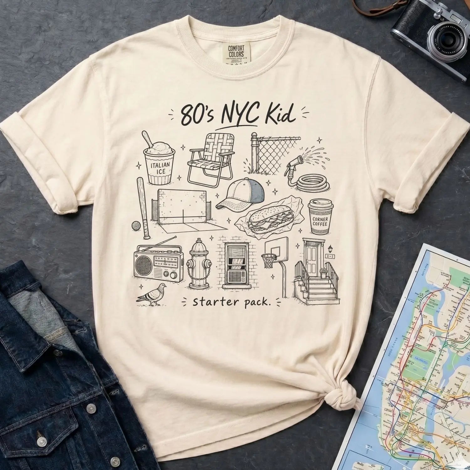 Ivory Comfort Colors t-shirt with '80's NYC Kid' graphic design on a dark surface with denim jacket and map.