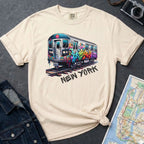 Ivory Comfort Colors t-shirt with a graffiti train graphic and 'New York' text  on a dark surface with a denim jacket and a map.