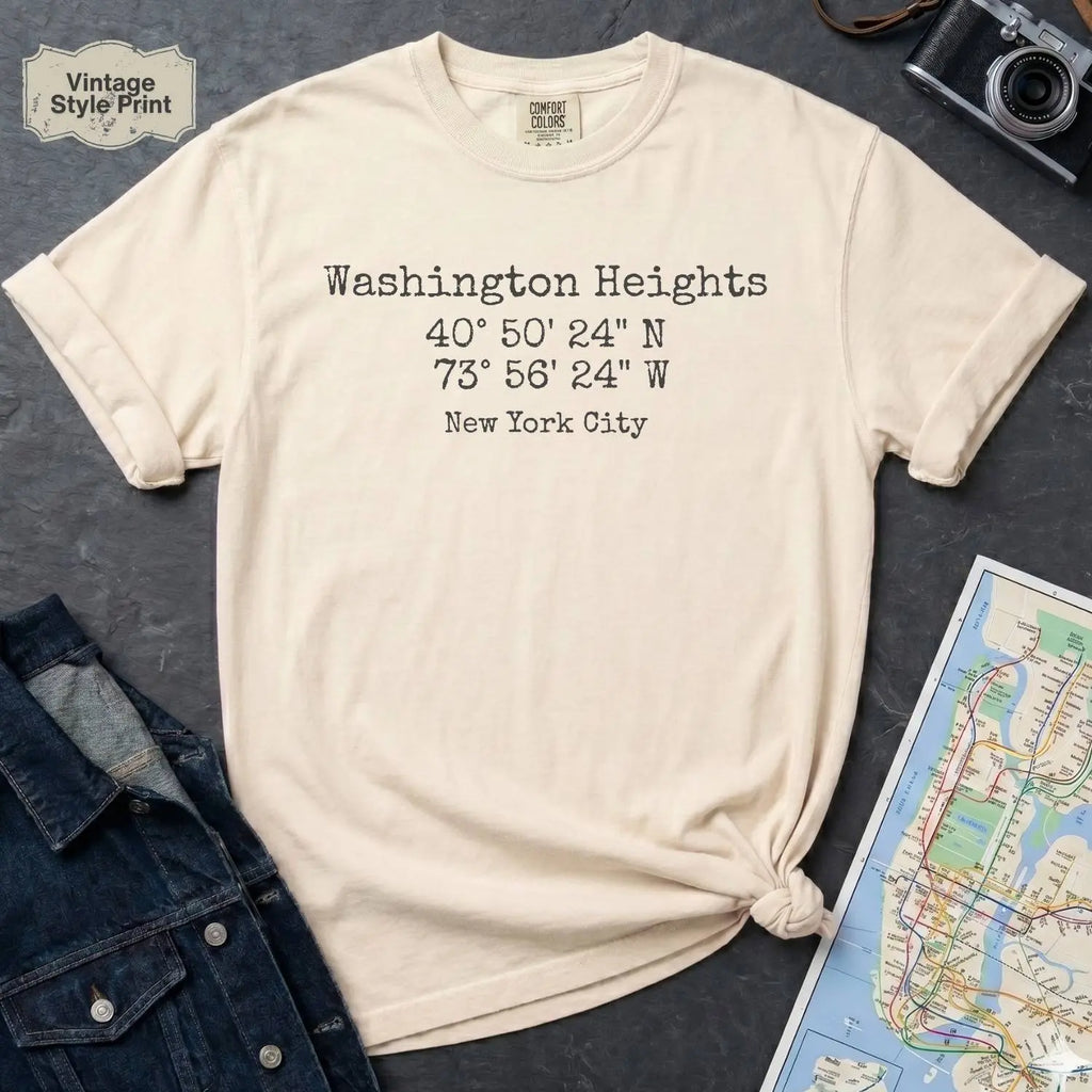 Ivory colored Comfort Colors t-shirt with 'Washington Heights' text with coordinates and 'New York City' on a dark surface with a map and denim jacket.