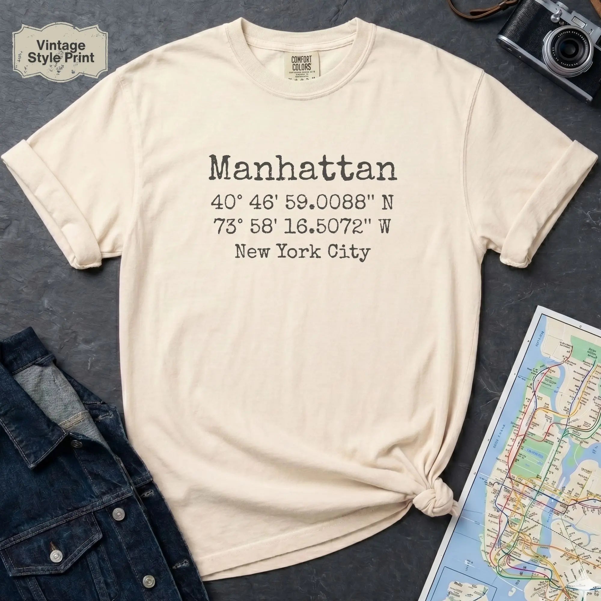 Beige t-shirt with Manhattan coordinates print, denim jacket, and map on a dark surface