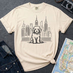 Ivory Comfort Colors t-shirt with a Golden Doodle and cityscape graphic on a dark surface with a denim jacket and a map.