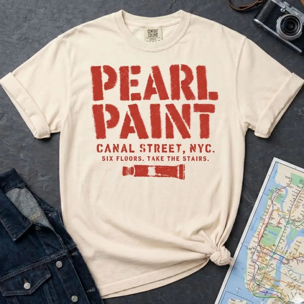 Ivory Comfort Colors t-shirt with Pearl Paint in large distressed stencil lettering, Canal Street NYC and Six Floors Take The Stairs below, with a paint tube graphic, displayed on a flat surface with a denim jacket and subway map in the background.