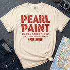 Ivory Comfort Colors t-shirt with Pearl Paint in large distressed stencil lettering, Canal Street NYC and Six Floors Take The Stairs below, with a paint tube graphic, displayed on a flat surface with a denim jacket and subway map in the background.