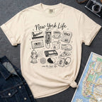 Ivory t-shirt with New York-themed graphics on a gray surface with a map and camera.