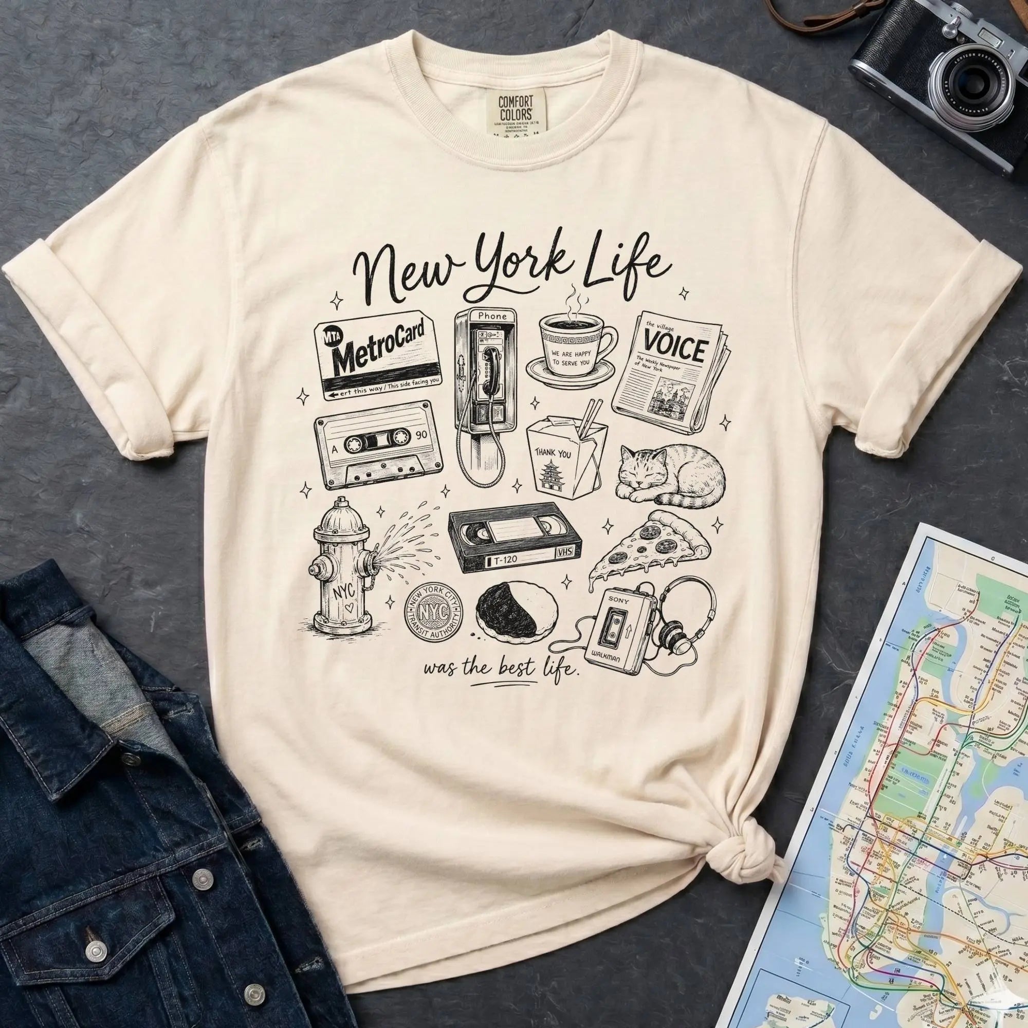 Ivory t-shirt with New York-themed graphics on a gray surface with a map and camera.