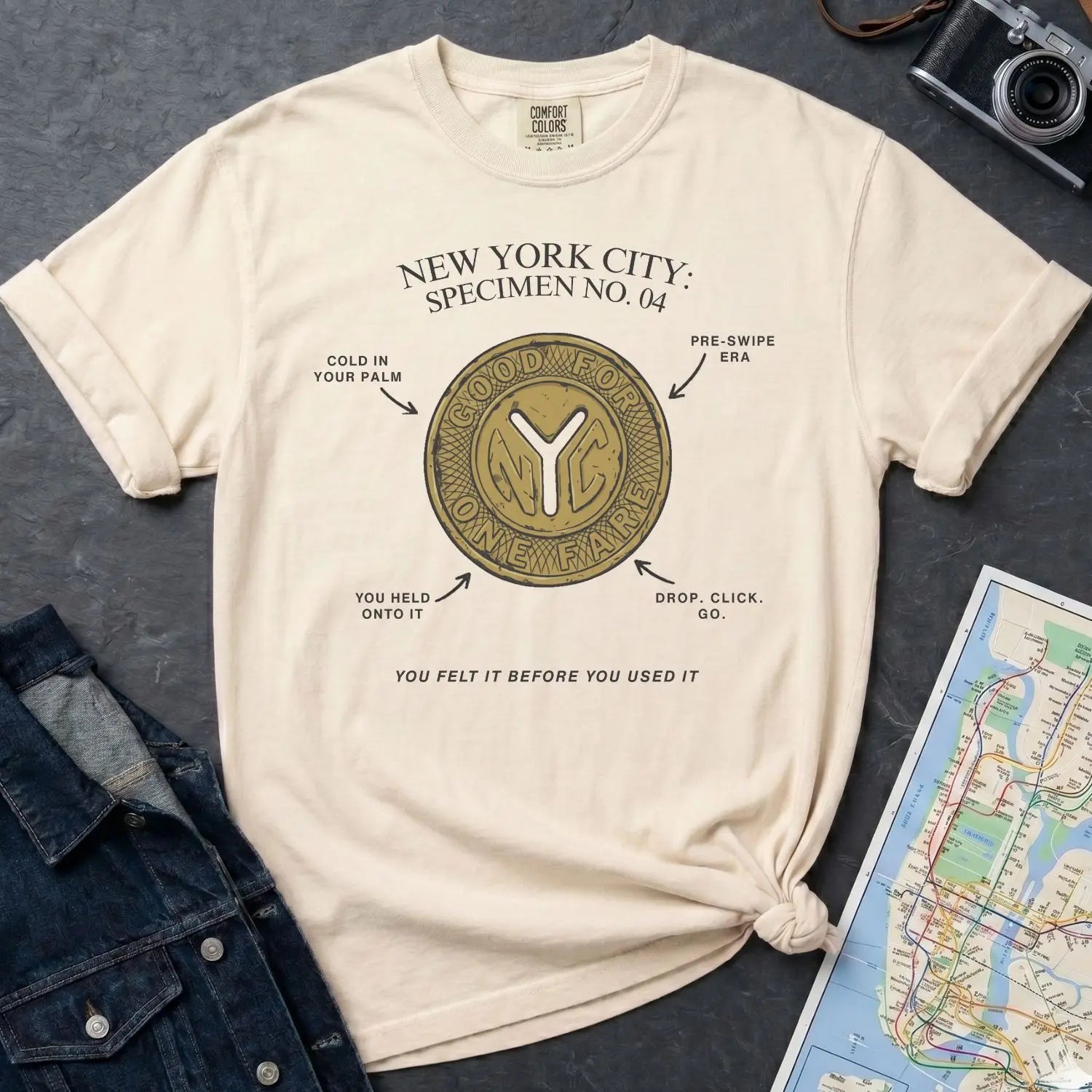 Ivory Comfort Colors t-shirt with New York City vintage token design on a gray surface with denim jacket and map.
