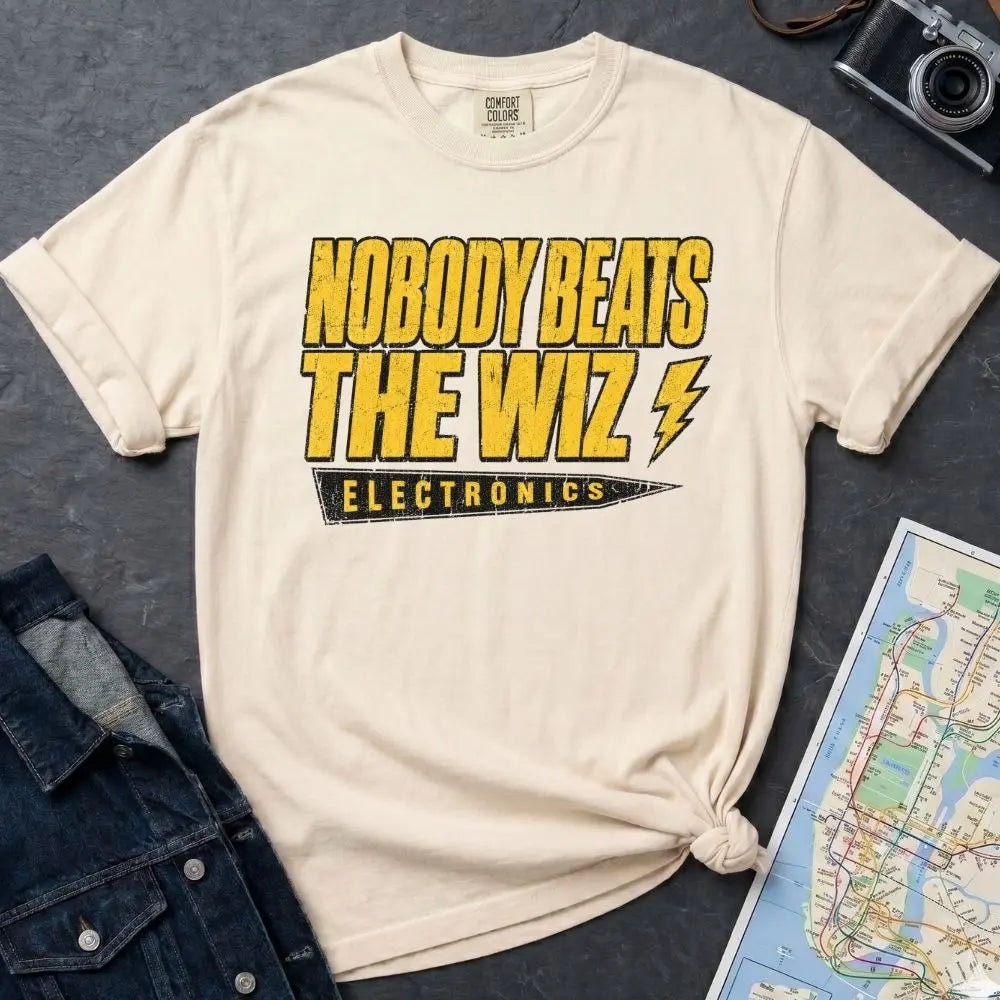 Ivory Comfort Colors T-shirt with yellow and black The Wiz Electronics NYC front print, styled with denim jacket, camera, and subway map