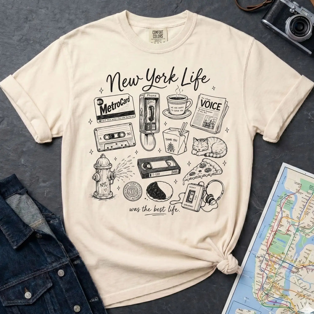 Ivory Comfort Colors t-shirt featuring a New York Life Was the Best Life graphic with hand-drawn NYC nostalgia icons including a MetroCard, cassette tape, pay phone, coffee cup, newspaper, pizza slice, fire hydrant, Walkman, and bodega cat.