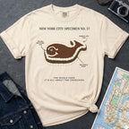 Ivory Comfort Colors T-shirt with NYC whale cake specimen front print, styled with denim jacket, camera, and subway map