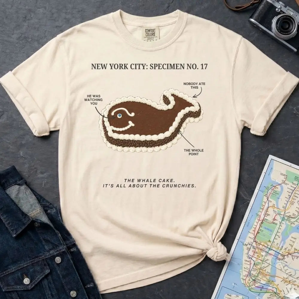 Ivory Comfort Colors T-shirt with NYC whale cake specimen front print, styled with denim jacket, camera, and subway map