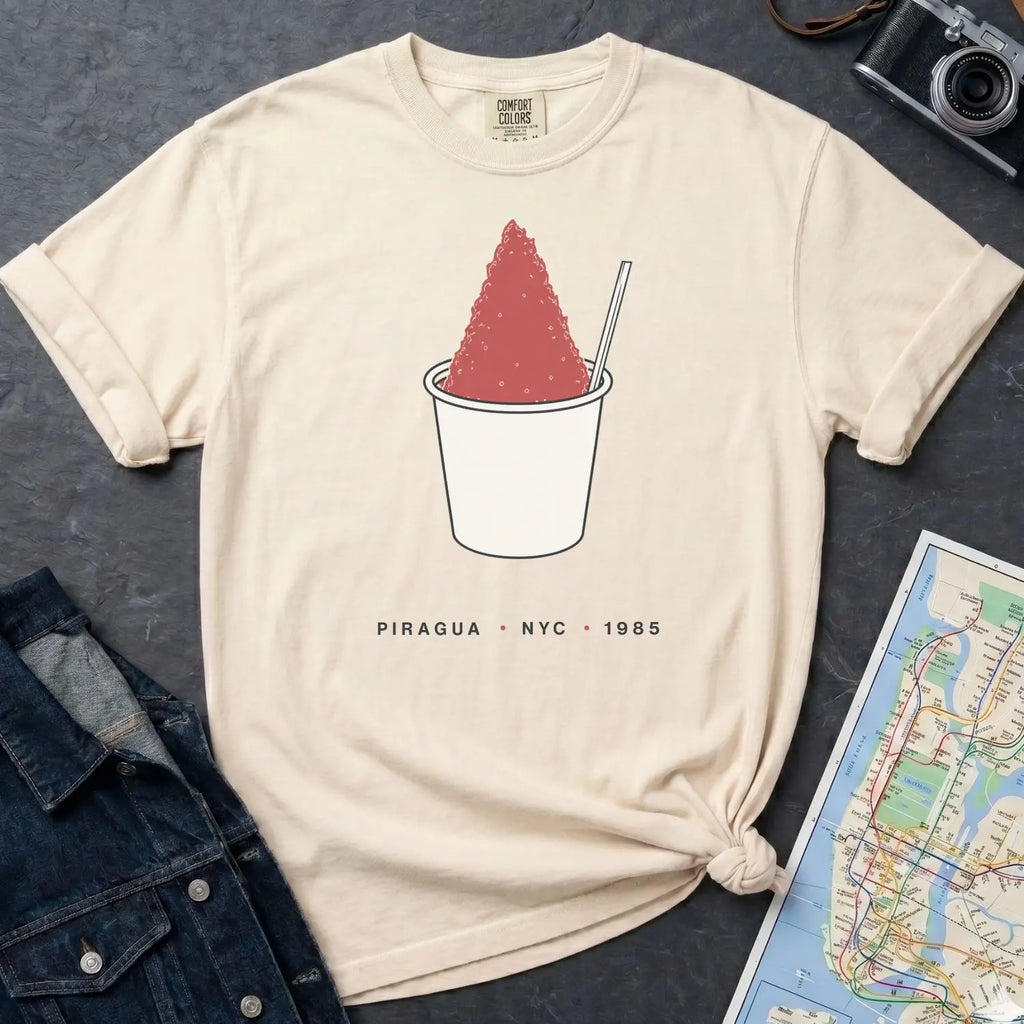 Ivory Comfort Colors t-shirt with a piragua graphic and text, placed on a dark surface with a map and denim jacket.