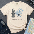 Ivory Comfort Colors t-shirt featuring a vintage NYC fire hydrant spraying water with “Summer Days • NYC • 1981” text, placed on a dark surface with a denim jacket and a map.