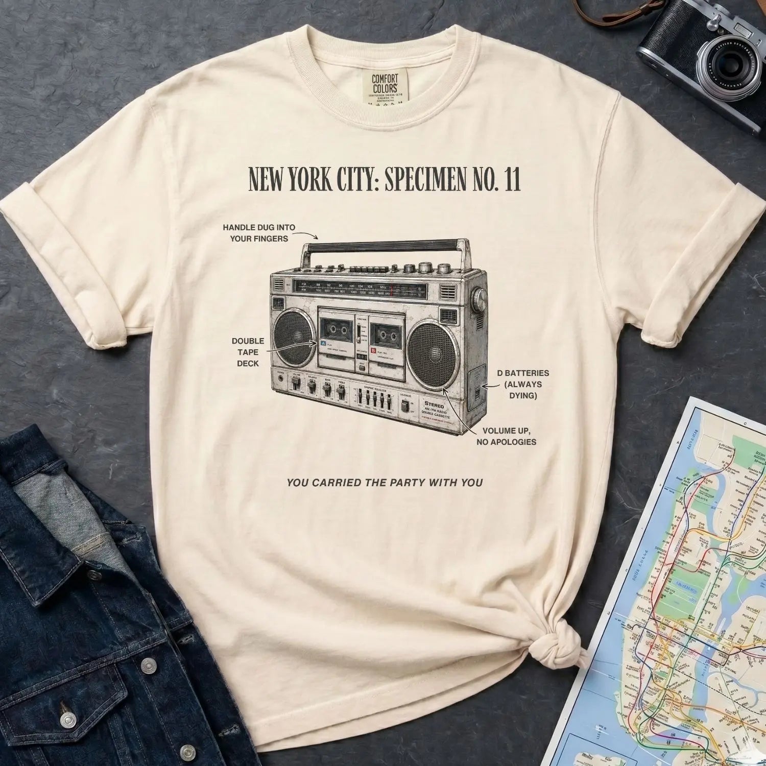 Ivory Comfort Colors t-shirt with a graphic of a boombox and text on a dark surface with a denim jacket and map.
