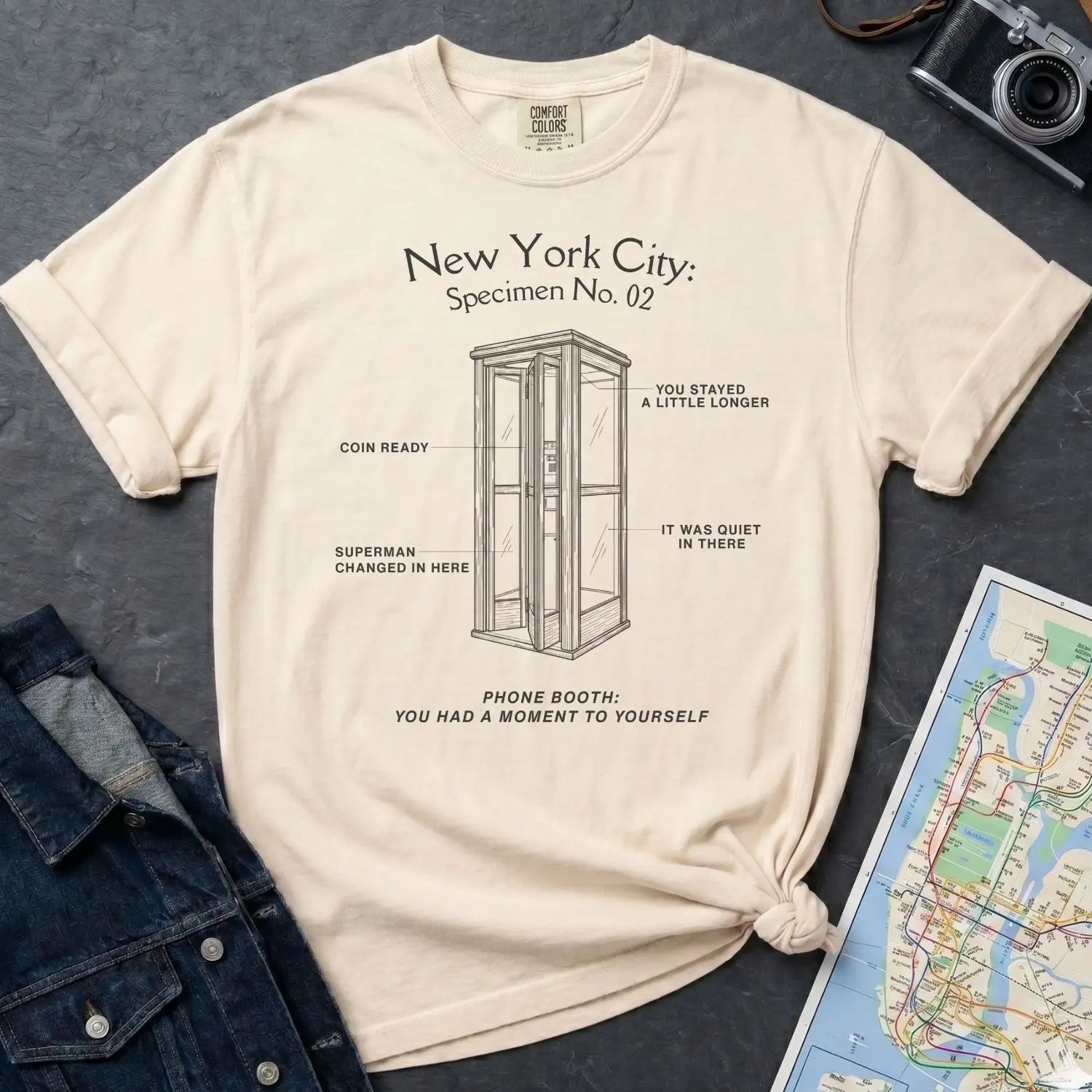 Ivory Comfort Colors t-shirt with phone booth design and text on a dark surface with denim jacket and map.