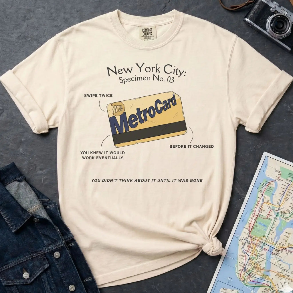 Ivory Comfort Colors t-shirt with New York City MetroCard graphic on a gray surface with a map and jacket.