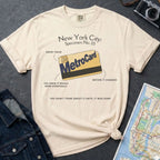 Ivory Comfort Colors t-shirt with New York City MetroCard graphic on a gray surface with a map and jacket.