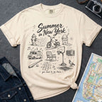 Ivory Comfort Colors t-shirt with 'Summer in New York' graphic design on a gray surface with denim jacket and map.