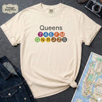 Beige t-shirt with 'Queens' and NYC subway lines on a dark surface with a map and denim jacket.