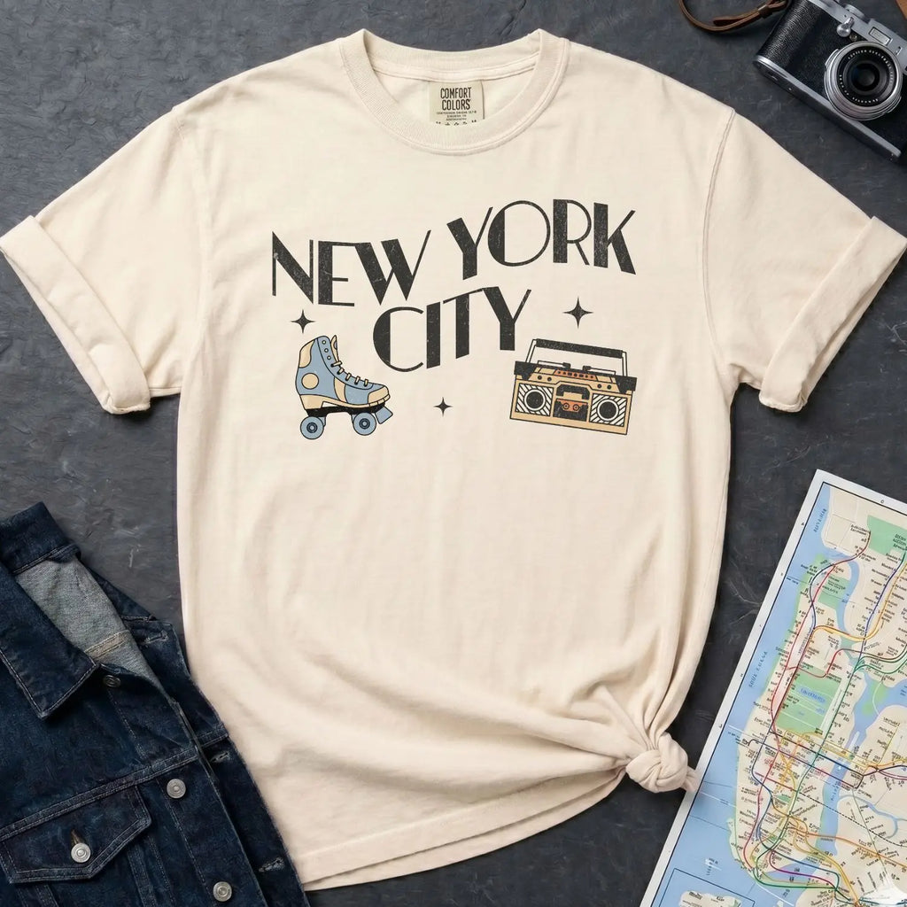Ivory Comfort Colors t-shirt with 'New York City' text and a roller skate and boom box on a dark surface with a denim jacket and a map.