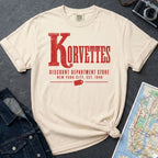 Ivory Comfort Colors t-shirt with Korvettes in large distressed vintage lettering, Discount Department Store and New York City, Est. 1948 below, with a price tag illustration, displayed flat with a denim jacket and subway map.