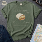 Green t-shirt with a graphic of a bodega sandwich and text on a dark surface with a map and jeans.