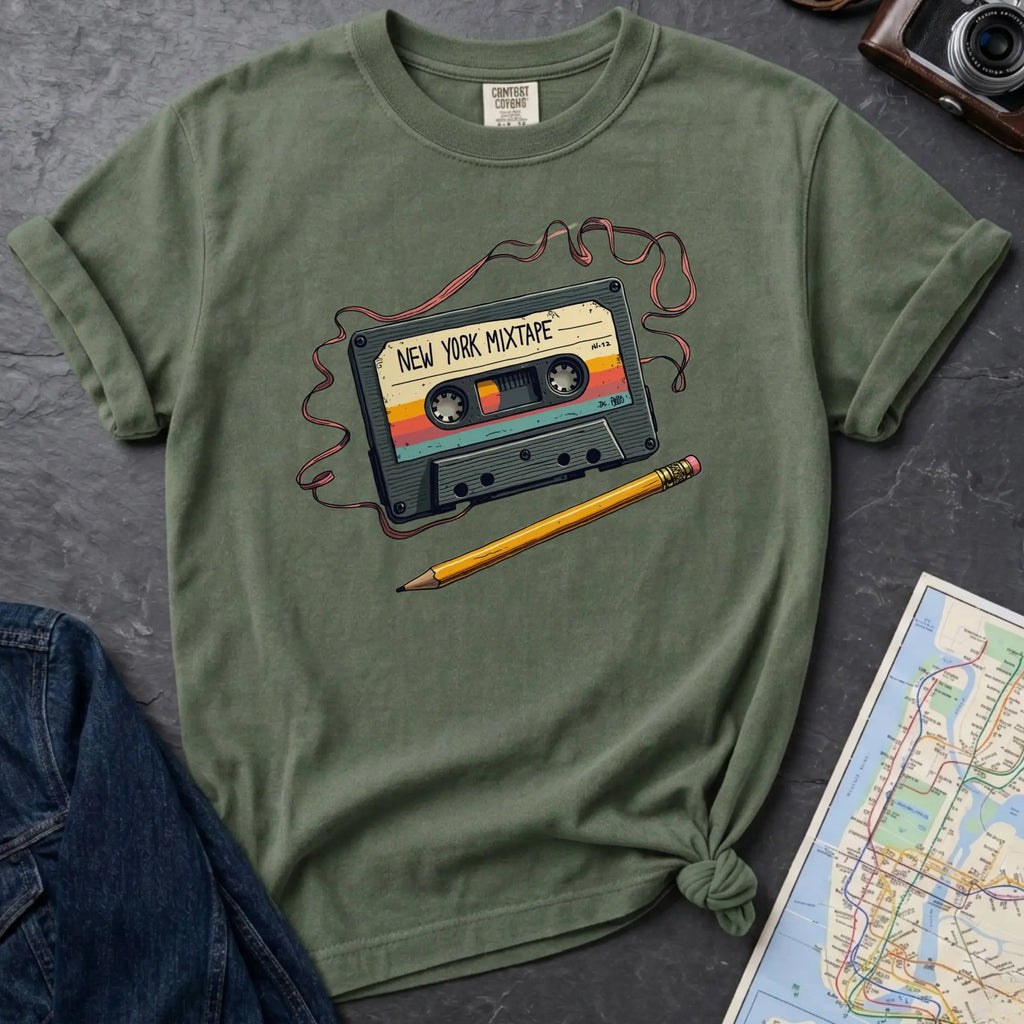 Moss green t-shirt with a cassette tape graphic and pencil on a gray surface with denim jacket and map.