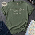 Moss colored t-shirt with text 'prospect park our first kiss' on a dark surface with a map and denim jacket.