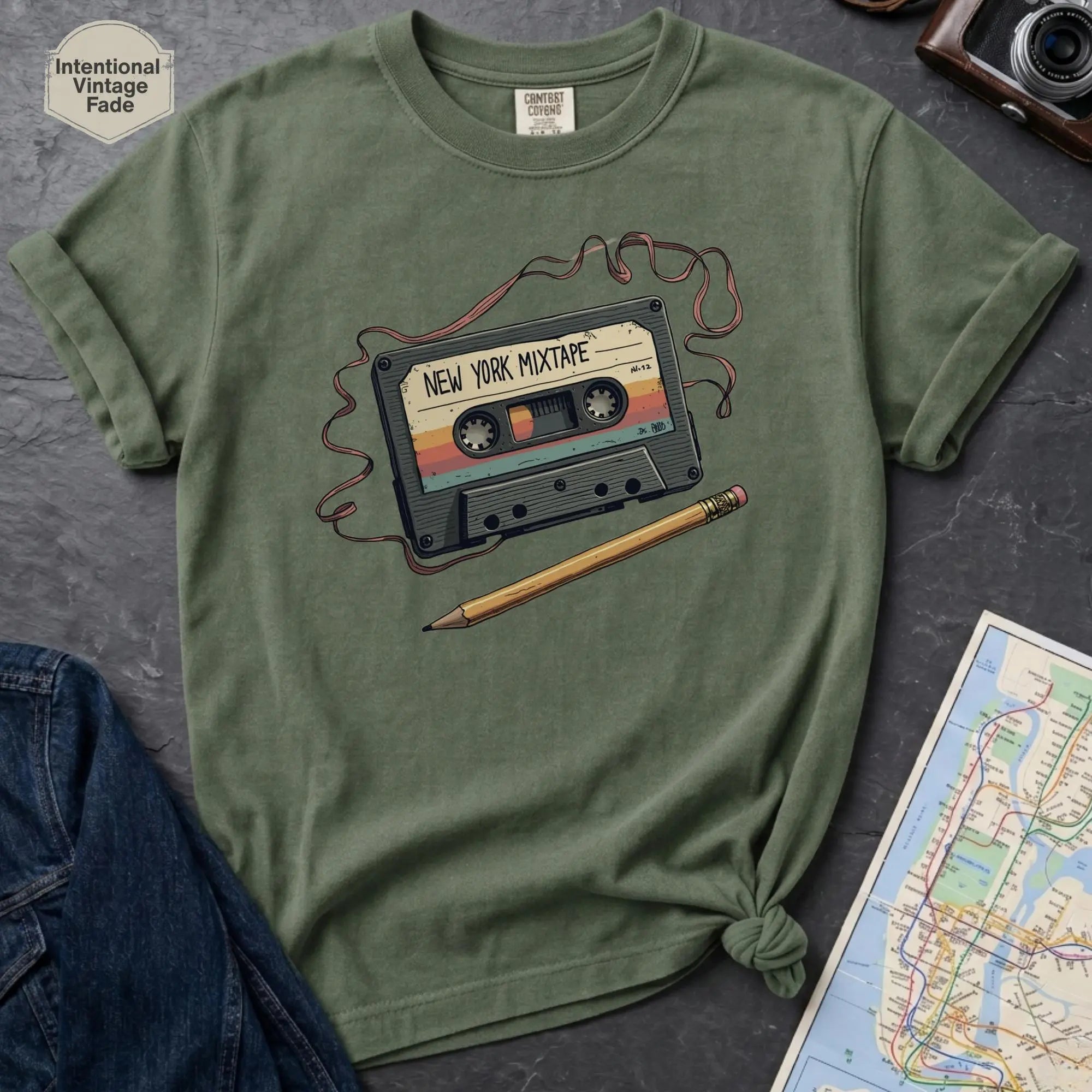 Green t-shirt with a cassette tape design on a dark surface with a map and camera.