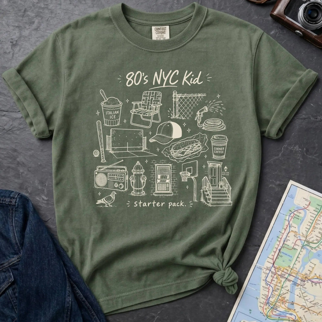 Moss green Comfort Colors t-shirt with an 80’s NYC Kid starter pack graphic featuring Italian ice, stickball, a fire hydrant, corner coffee, and stoop illustrations.