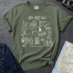 Moss green Comfort Colors t-shirt with an 80’s NYC Kid starter pack graphic featuring Italian ice, stickball, a fire hydrant, corner coffee, and stoop illustrations.