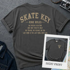 Pepper colored Comfort Colors t-shirt, back view, with Skate Key Rink Rules printed in distressed gold lettering. Rules read: No Rough Skating, One Way Traffic Only, No Trains No Chains No Tag, Last Song Is The Last Song Don't Ask. Inset shows shirt front with Skate Key Staff logo on chest.