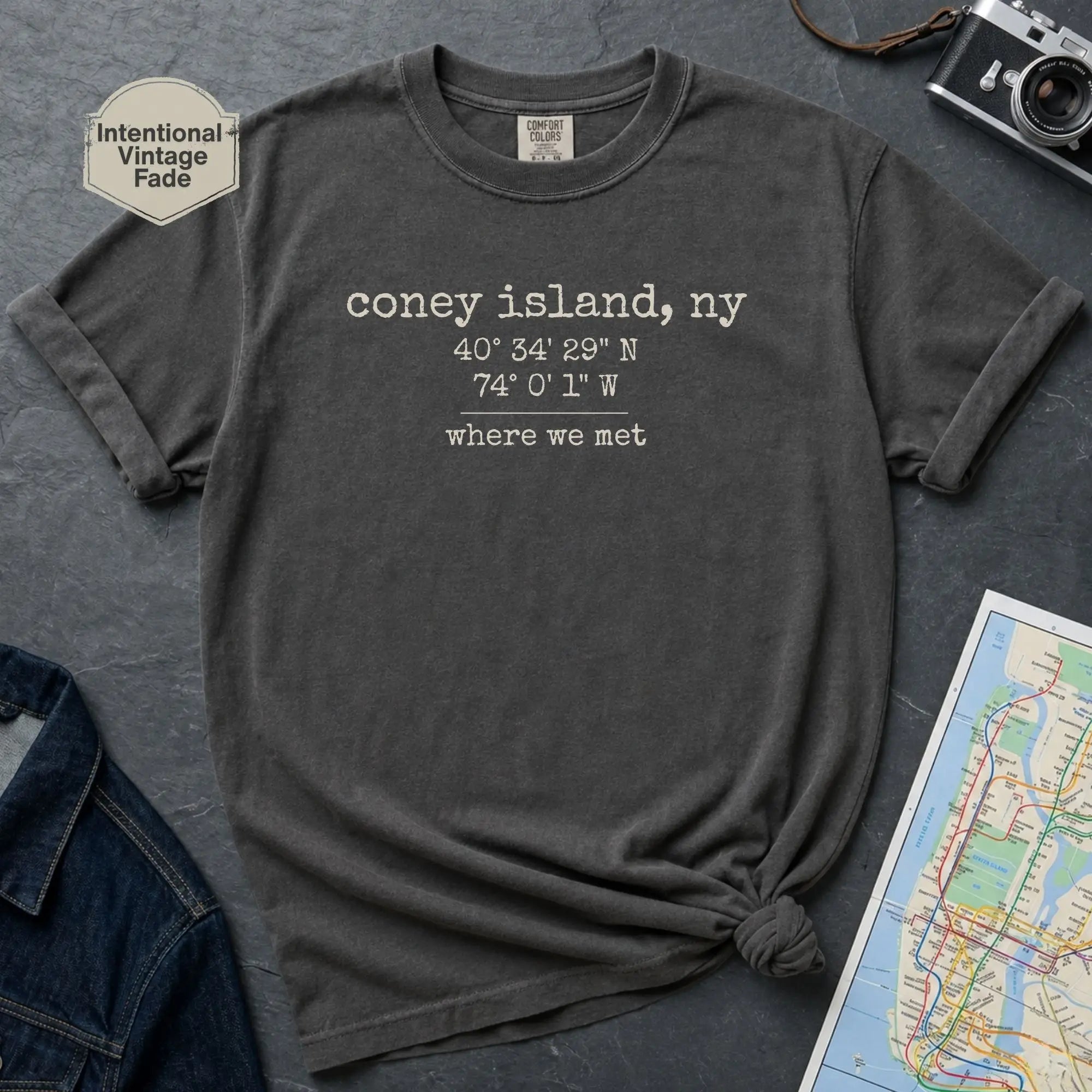Dark gray t-shirt with 'Coney Island, NY' text on a gray surface with a map and camera.