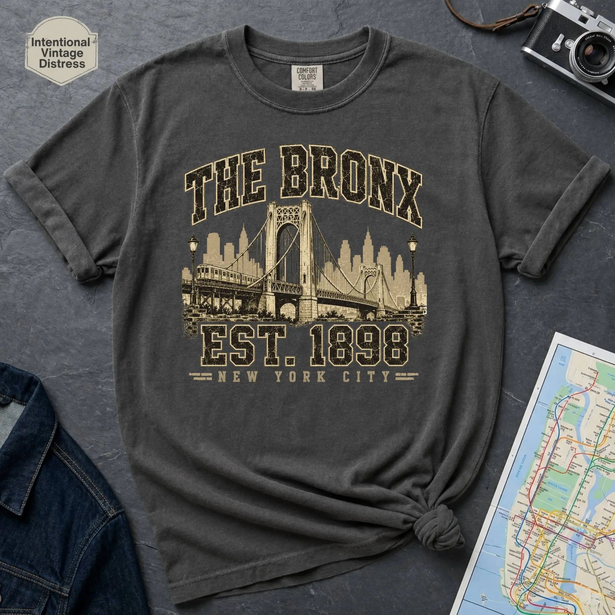 Pepper colored t-shirt with 'The Bronx Est. 1898' design on a dark surface with a map and a denim jacket.