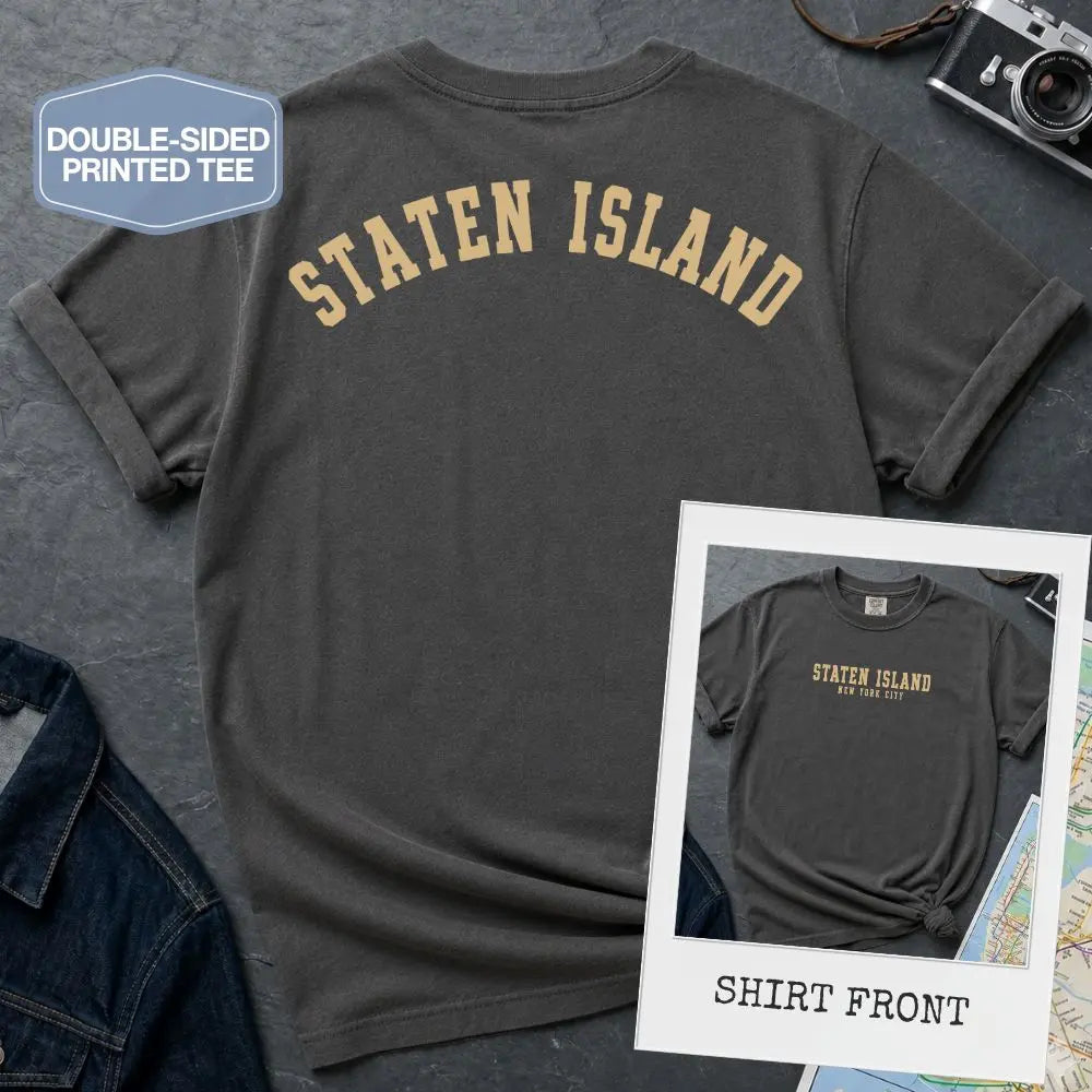 Pepper colored Comfort Colors t-shirt with 'Staten Island' text on a textured surface with a camera and denim jacket.